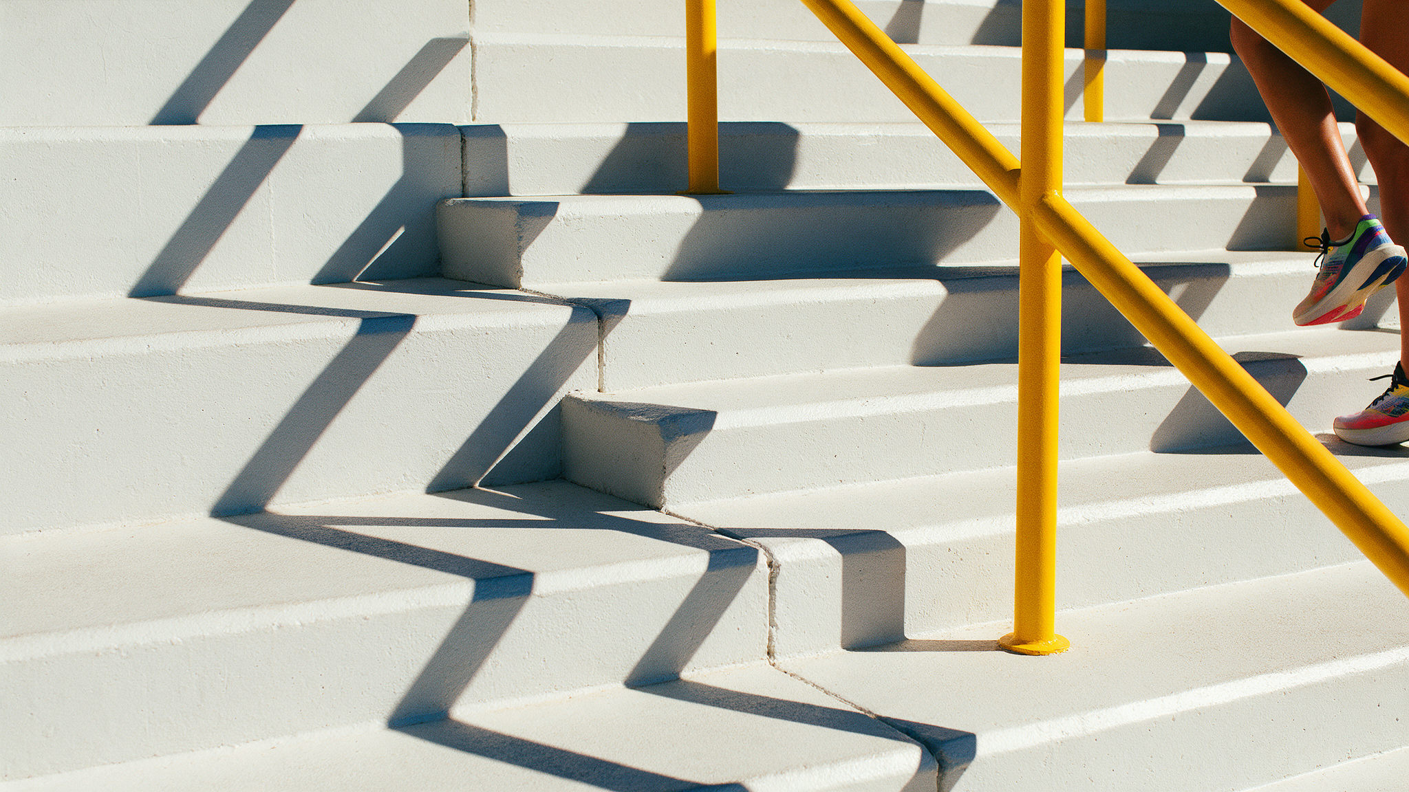 Bright sunlit concrete stairs with a bold yellow handrail and crisp graphic shadows