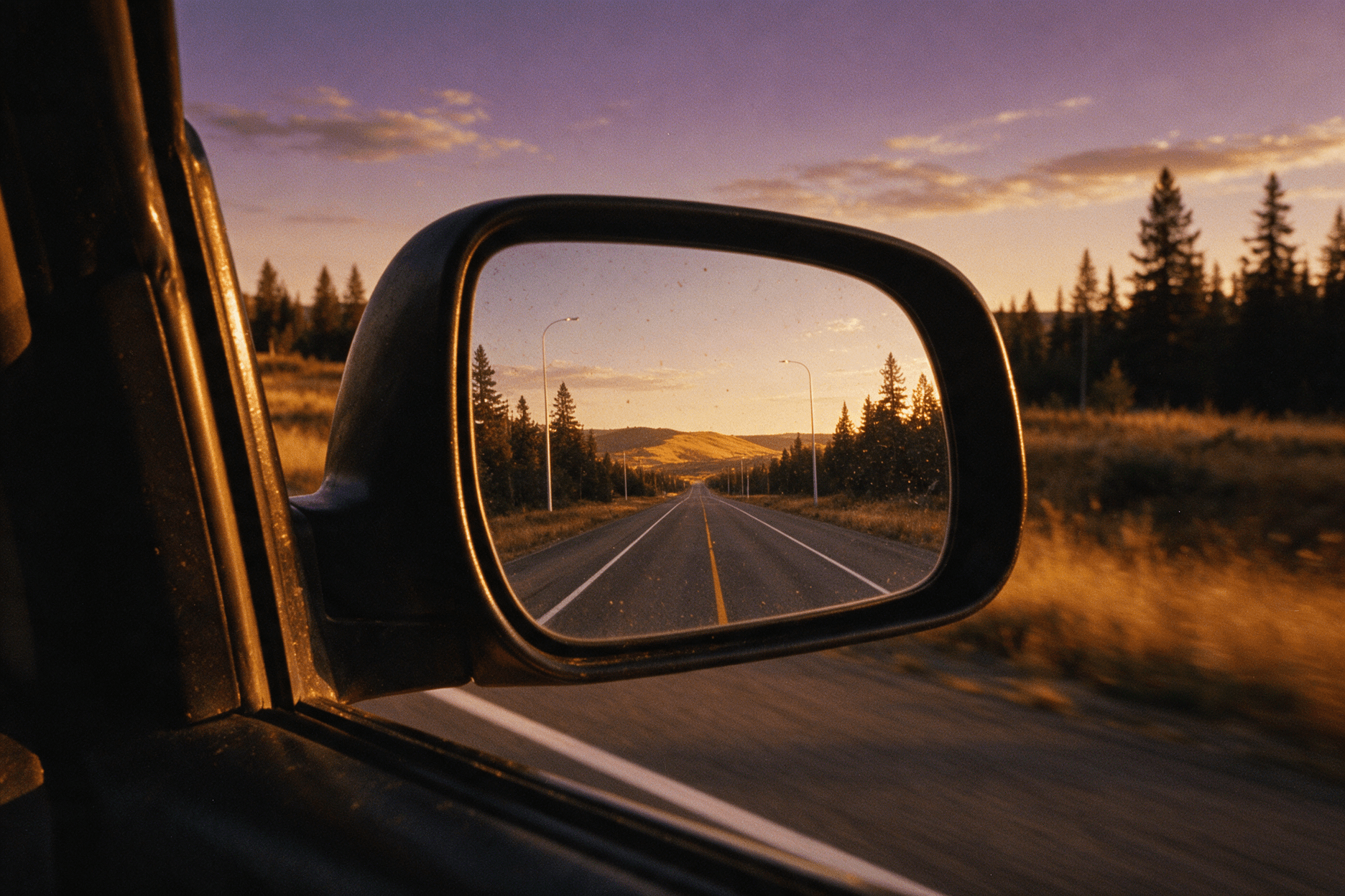 A car side mirror at dusk reflecting the empty road already travelled behind